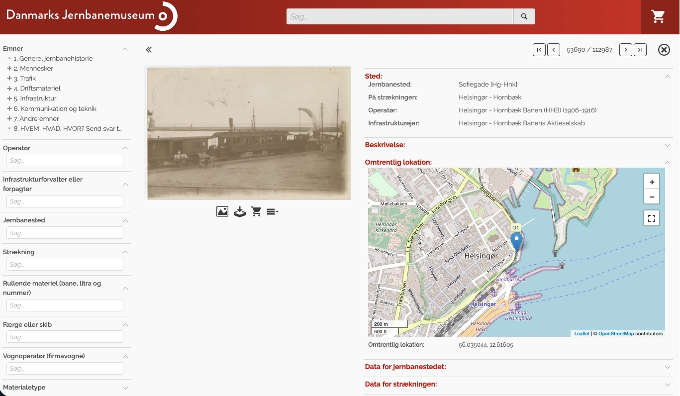 Infokort i Danmarks Jernbanemuseums portal. Til venstre det samme søgepanel; i midten et historisk fotografi af en dampfærge ved kaj; til højre felterne under Sted med jernbanestedet Sofiegade, strækningen Helsingør — Hornbæk og operatøren Helsingør - Hornbæk Banen (1906-1916), og under dem et udsnitskort med lokationen markeret ved Helsingør og koordinaterne 56.035044, 12.61605. Tælleren øverst viser emne 53.690 af 112.987.